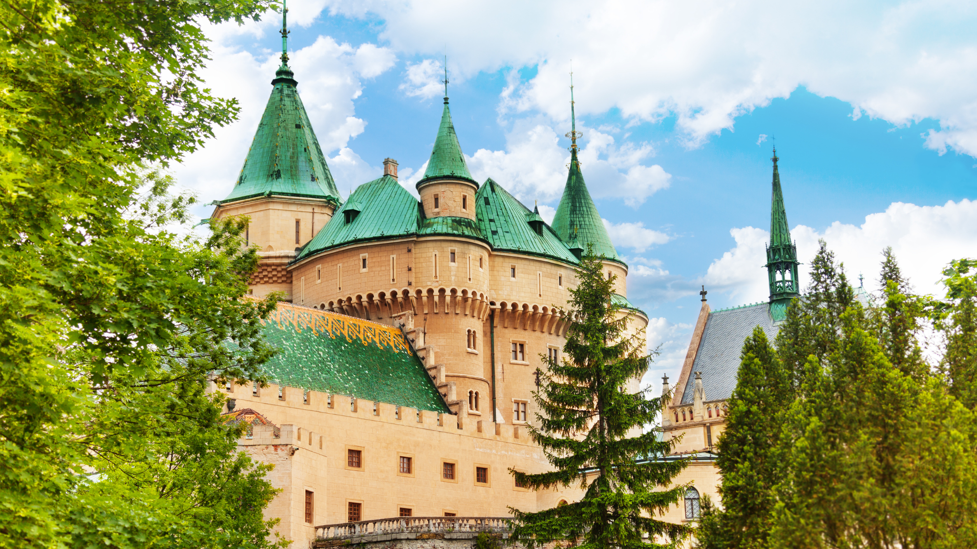 Bojnice Castle with blue roofs seen through evergreen trees and clear skies