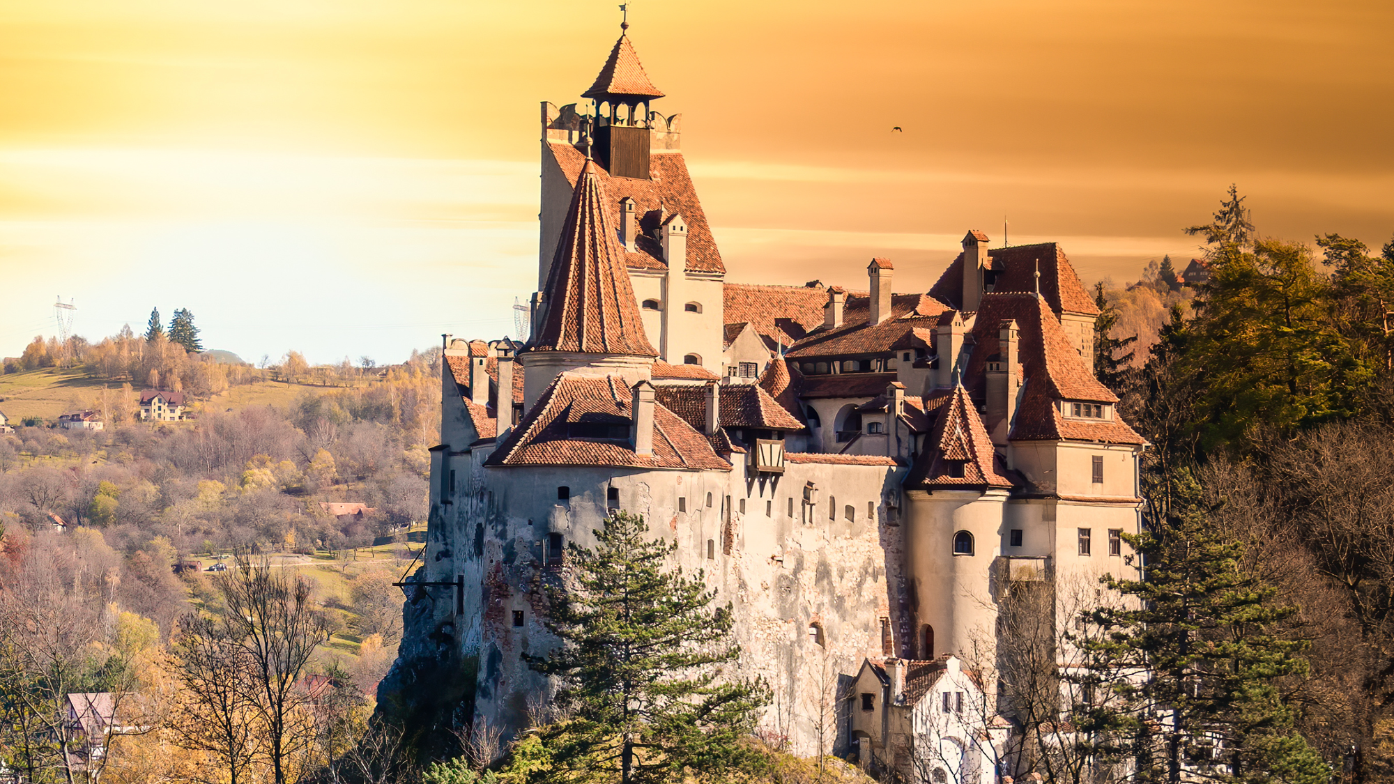 *"Bran Castle in Romania, surrounded by autumn trees with an orange haze in the sky, adding a mysterious atmosphere."*