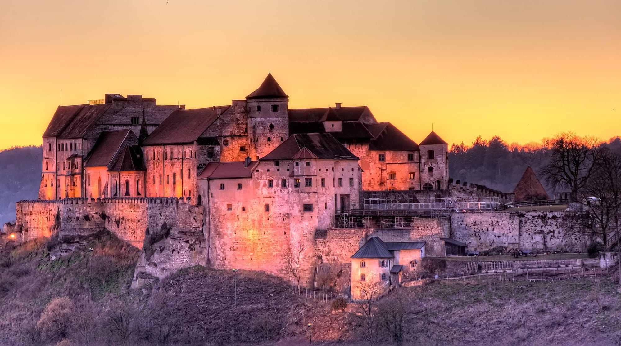 Burghausen Castle in Germany, glowing in the sunset with snow-covered grounds and its long medieval walls stretching across the winter landscape.