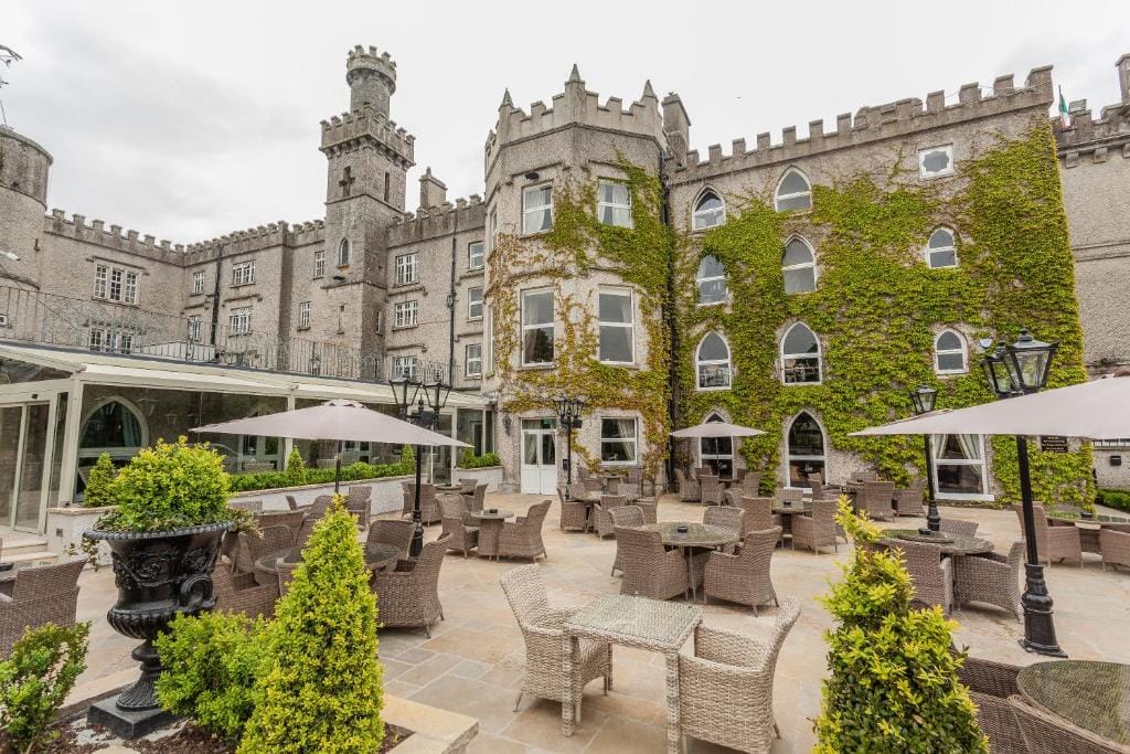 Cabra Castle in the Cabra neighborhood of Dublin, featuring ivy-covered stone walls, Gothic-style windows, and an outdoor patio with elegant seating arrangements.