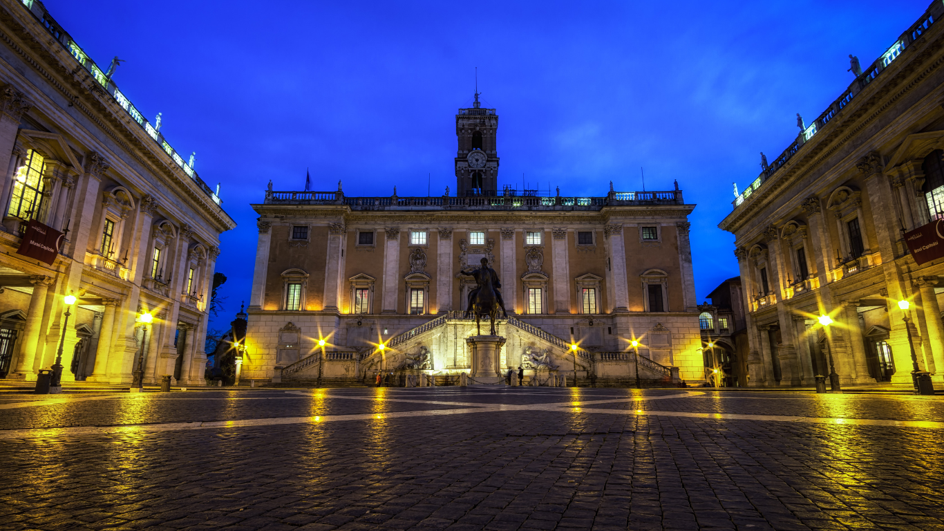 buildings in front of the Capitoline Museums in Rome, featuring classical Renaissance architecture. Each building has grand facades adorned with columns, arches, and statues. The central building, Palazzo Senatorio, is flanked by the Palazzo dei Conservatori and the Palazzo Nuovo, creating a symmetrical and impressive view. The spacious plaza in front of the buildings is lined with cobblestones and features Michelangelo's geometric design, adding to the historical grandeur of the site.