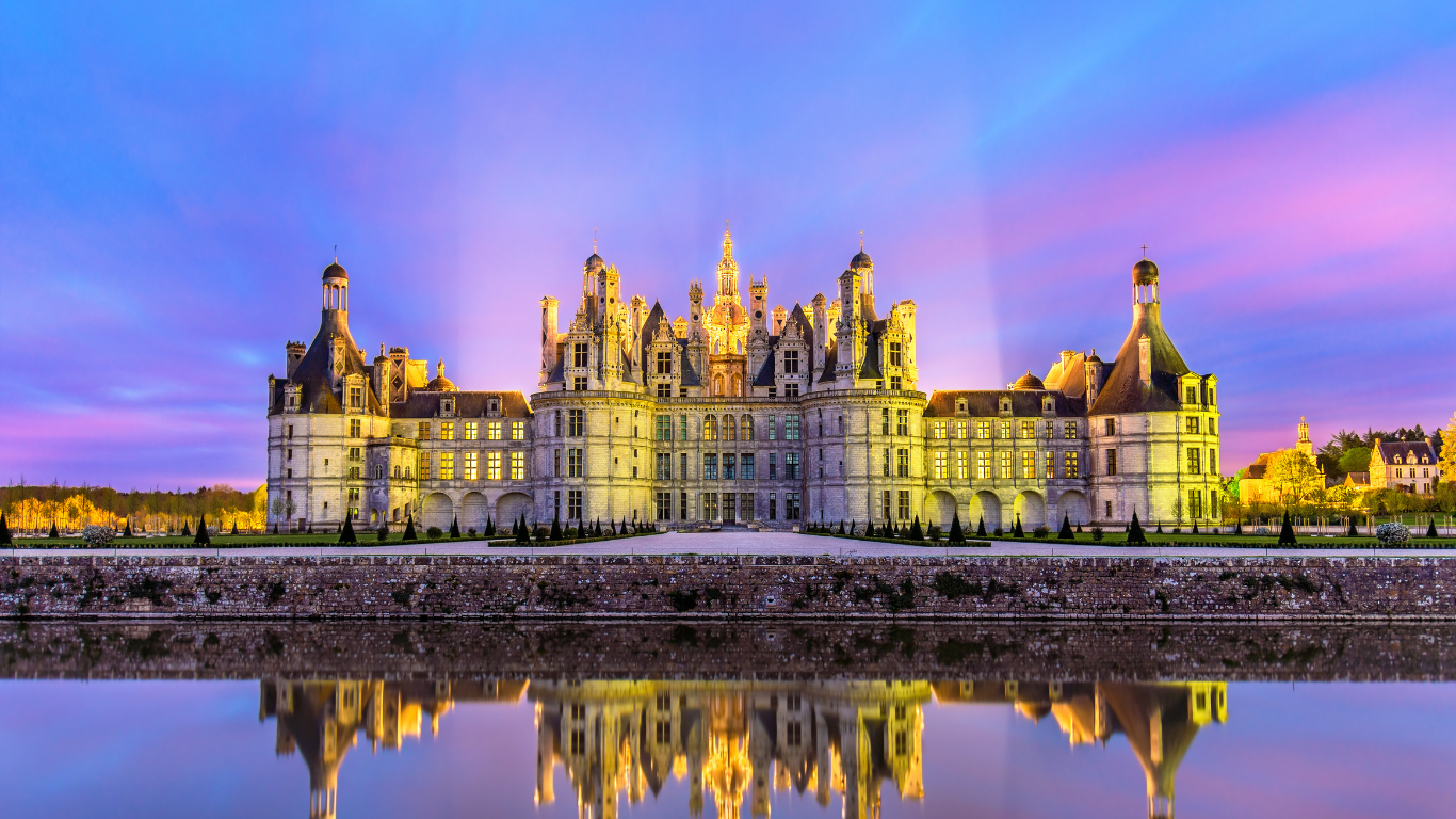 view from across the water of Château de Chambord in the eve with pretty blue and pink skies