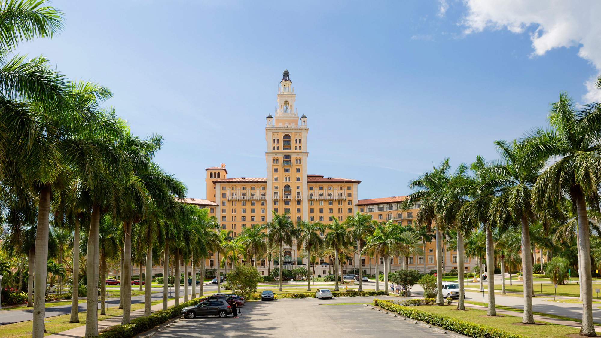 Grand view of the historic Biltmore Hotel in Coral Gables, Miami, framed by towering palm trees under a bright blue sky.