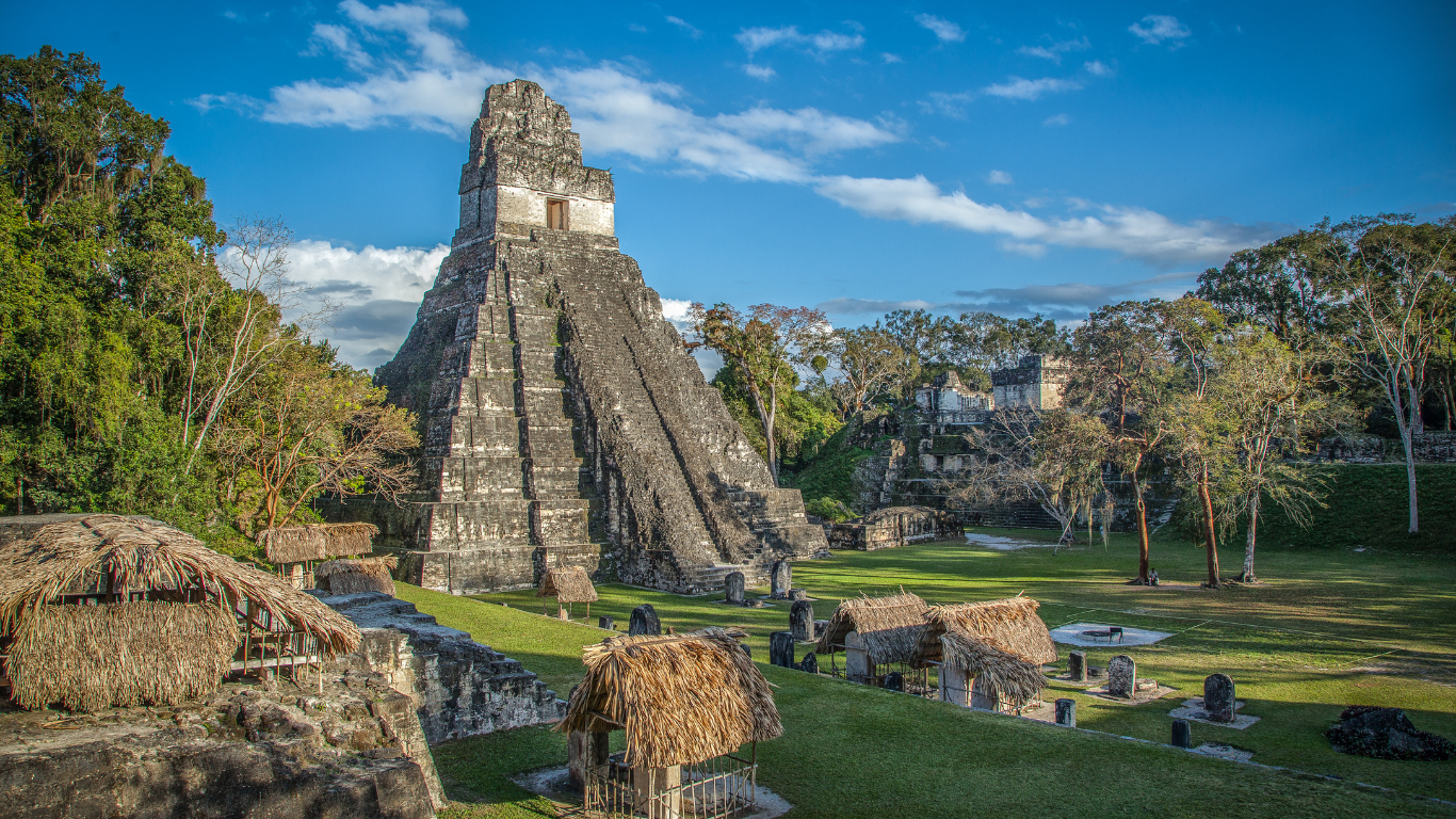 Mayan city at Tikal National Park Mayan Ruins that is a steep pyramid surrounded by trees and bright green grass.