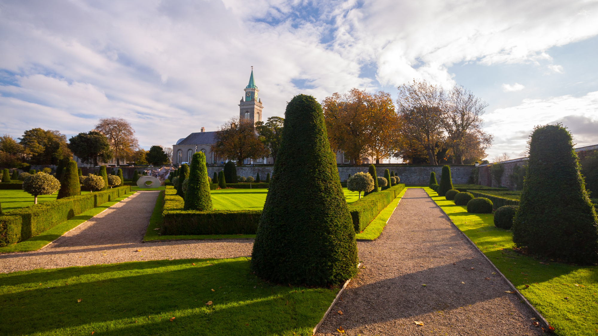 Kilmainham neighborhood in Dublin, Ireland, featuring a beautifully manicured garden with neatly trimmed hedges and a historic building in the background, under a partly cloudy sky.