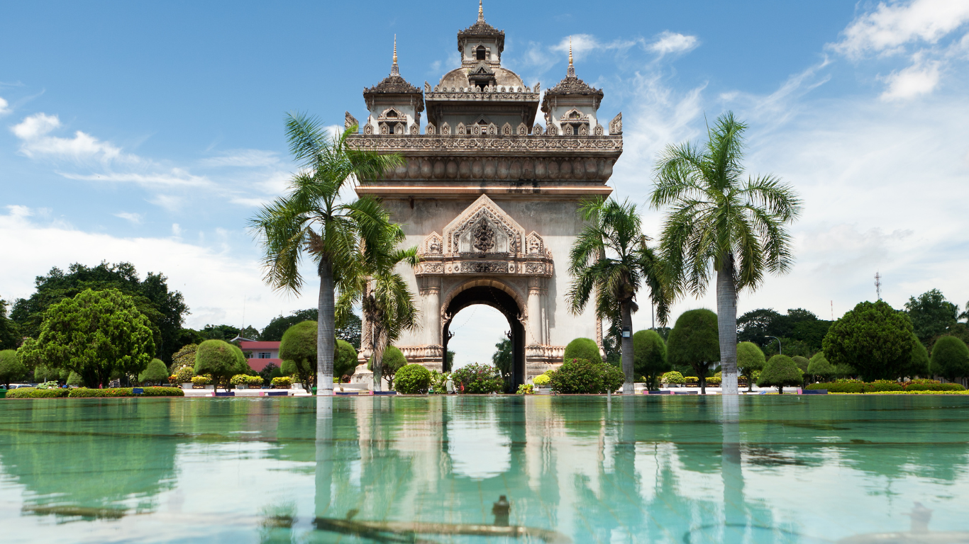 Clear waters with a beautiful arched monument surrounded by palm trees in Laos called Patuxai or Victory Gate 