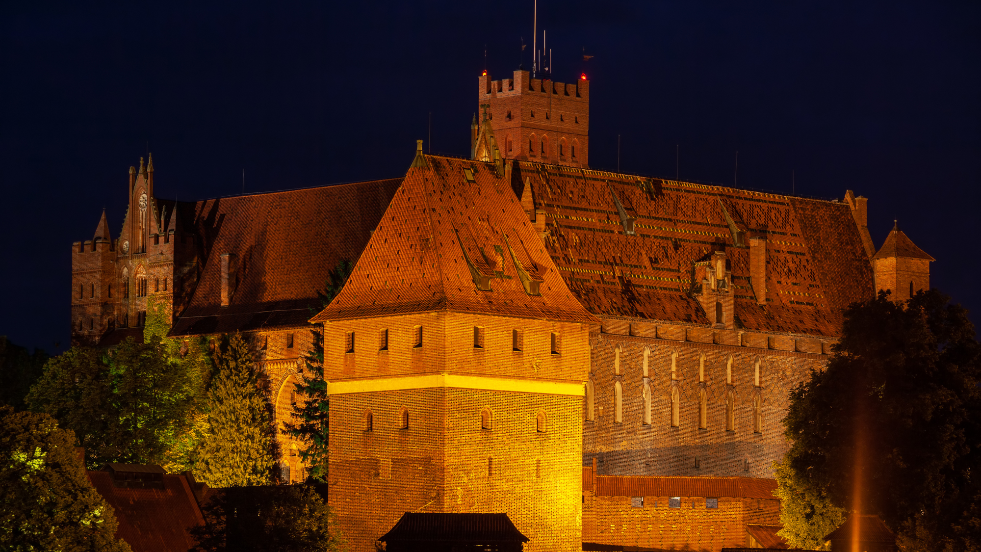 Malbork Castle in Poland illuminated at night, with lights highlighting its brick walls and Gothic architecture.