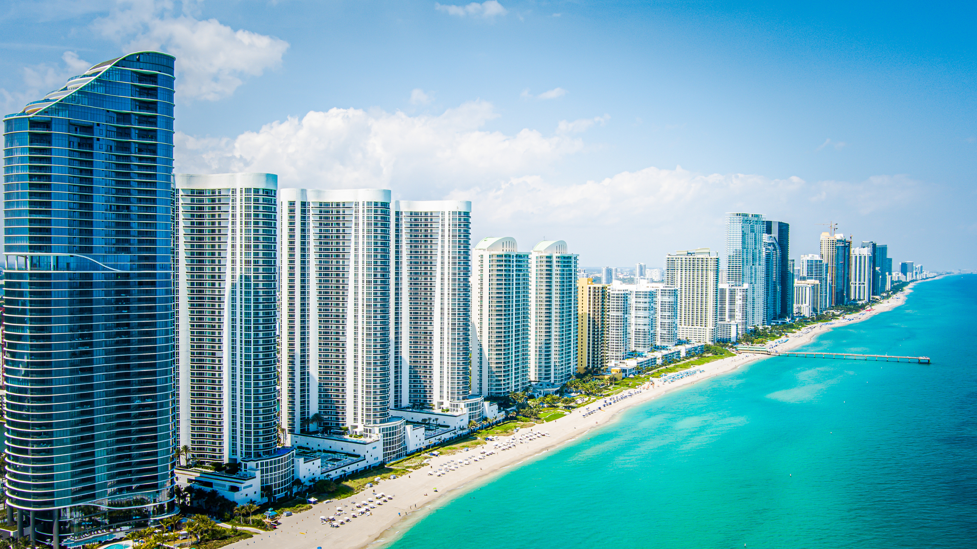 Skyscrapers line the pristine shoreline of Miami Beach, offering luxury beachfront accommodations with stunning views of the turquoise waters and white sandy beaches.