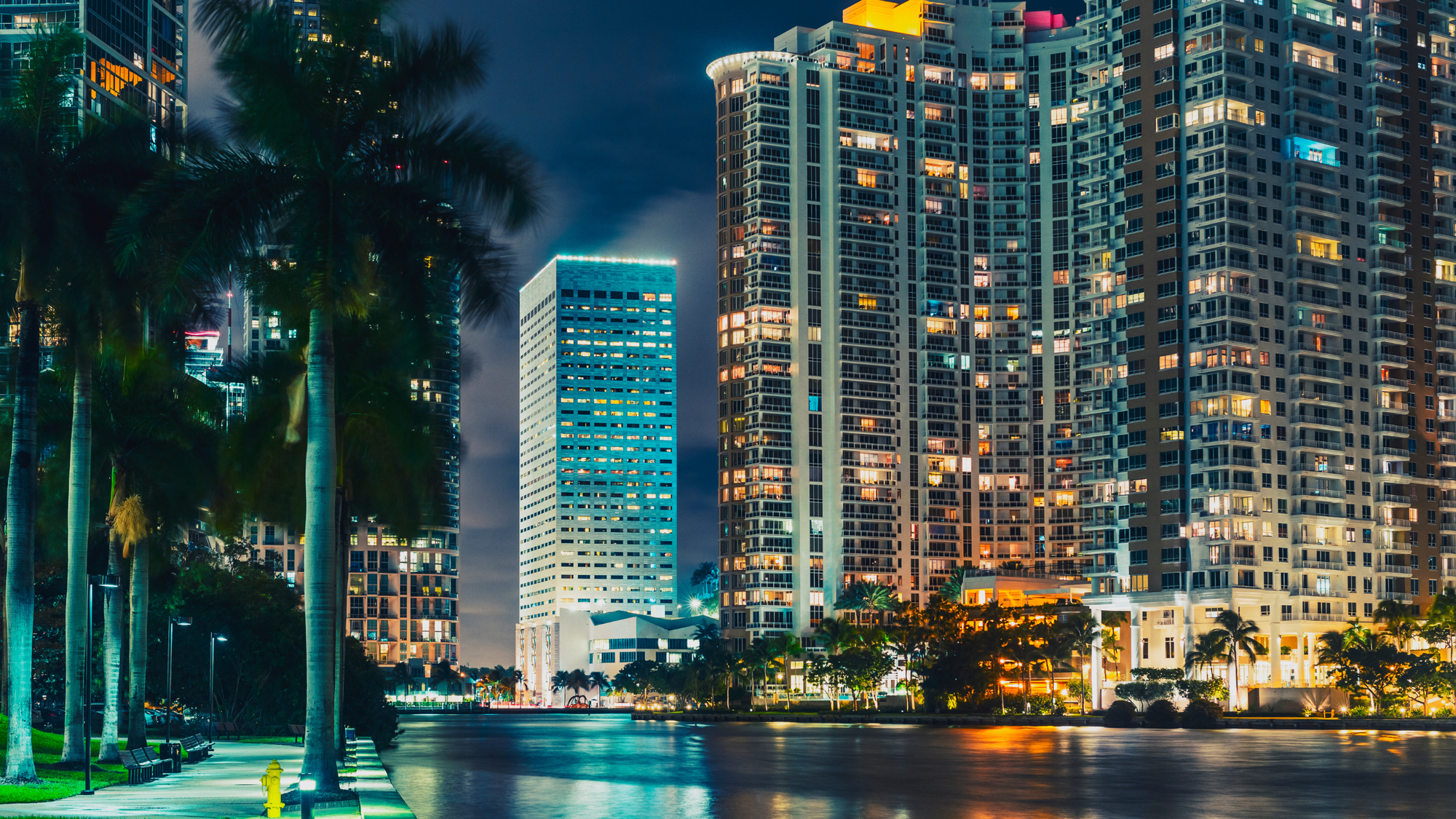 Nighttime view of the illuminated skyscrapers in Midtown Miami, Florida, with reflections shimmering on the waterfront, showcasing the vibrant cityscape.