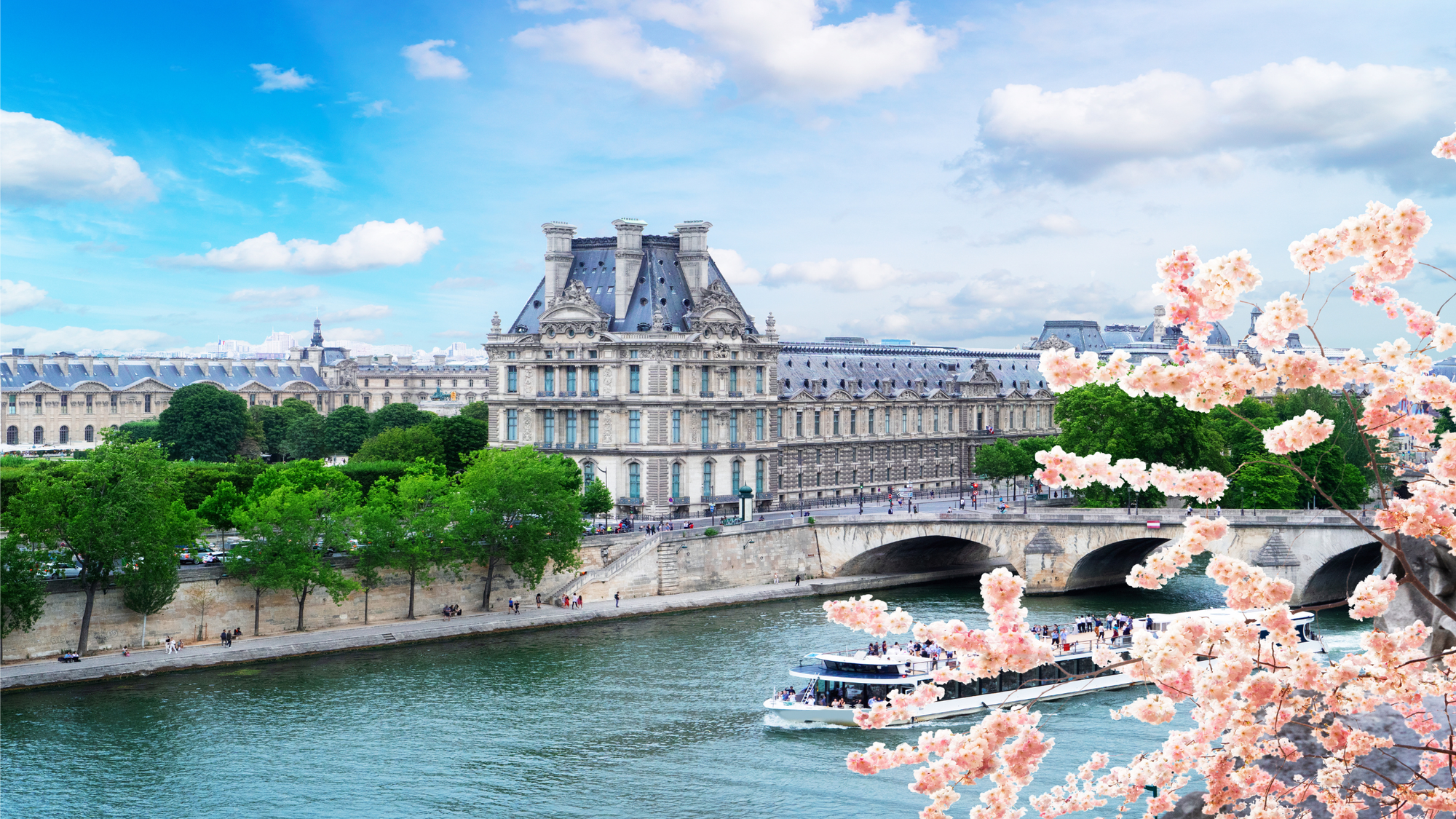 Musée d'Orsay museum is a large concrete building looks like a palace with Victorian style with blue on the roof from across the river with pink blooms on the trees