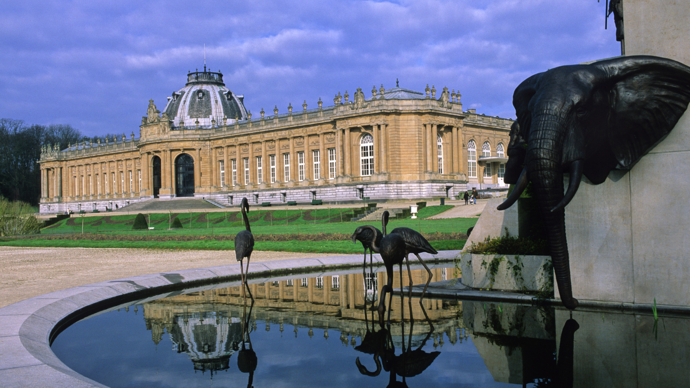 The Musée de l'Orangerie is a low, rectangular building with a classical design, featuring a light-colored stone facade and large arched windows. Nestled in the Tuileries Garden in Paris, it has a simple, elegant appearance, surrounded by trees and greenery. 