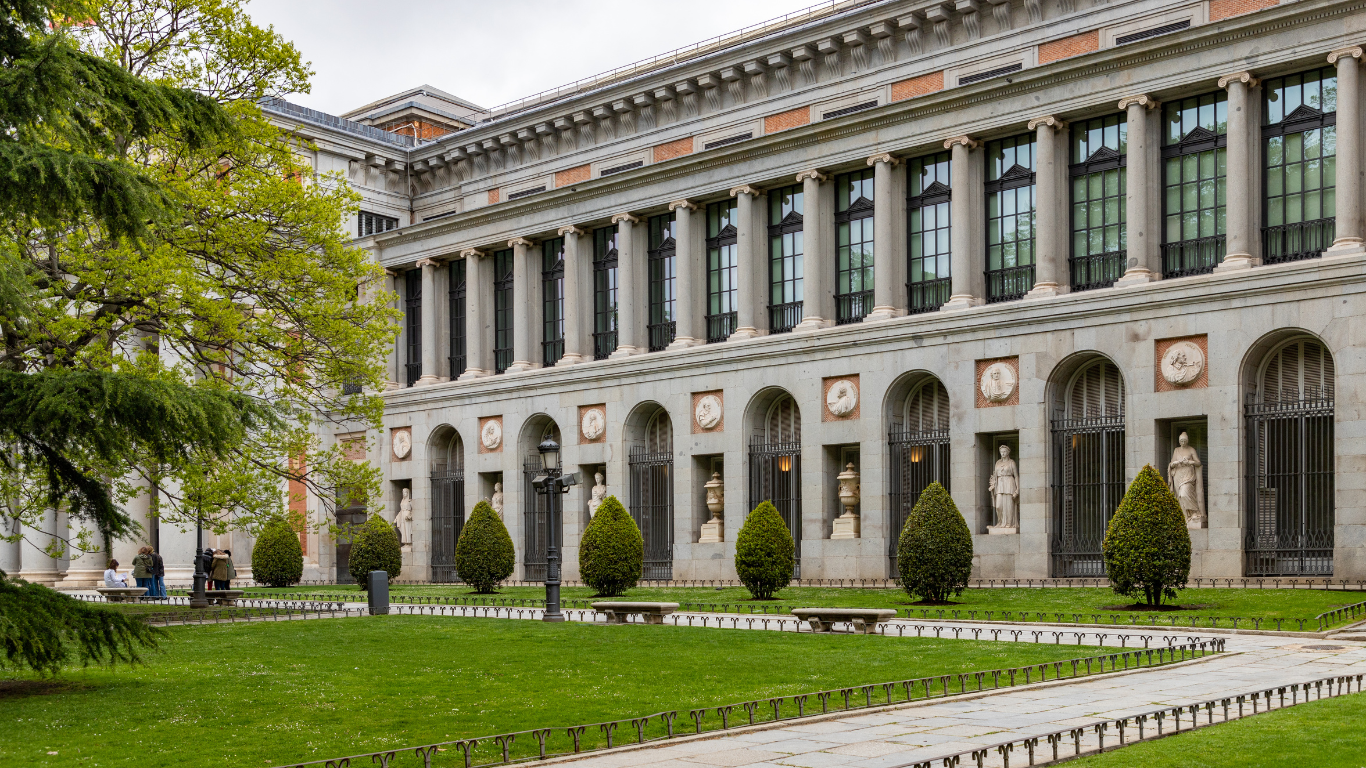 The National Roman Museum (Museo Nazionale Romano), housed in a historic building with a neoclassical facade in Rome. The structure features grand arched windows, ornate stone carvings, and a central entrance framed by columns. The museum's exterior reflects its cultural importance, showcasing Roman architectural heritage. The surrounding area is paved, with trees and historical landmarks nearby, creating a serene yet monumental atmosphere.