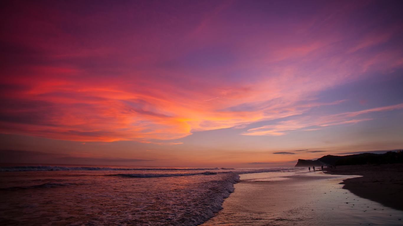 bright colorful skies of pink and purple at sunset on the beach with waves washing on to the shore in Nicaragua.