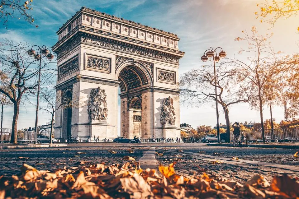 Arc de Triomphe in the fall with leaves on the ground and tourist taking photos