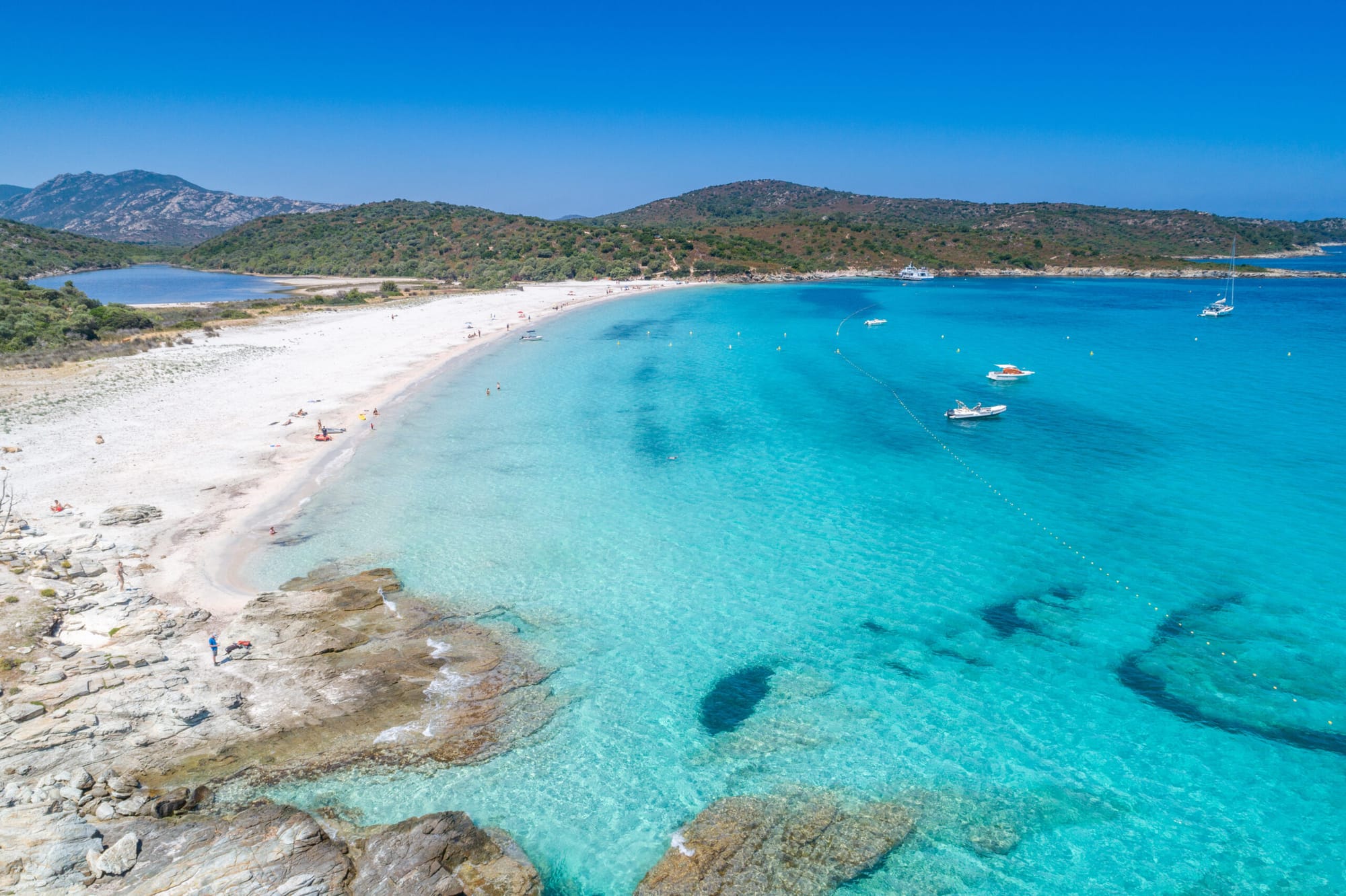 the clearest emerald water you've seen with white sandy shores with boats anchored near the shoreline