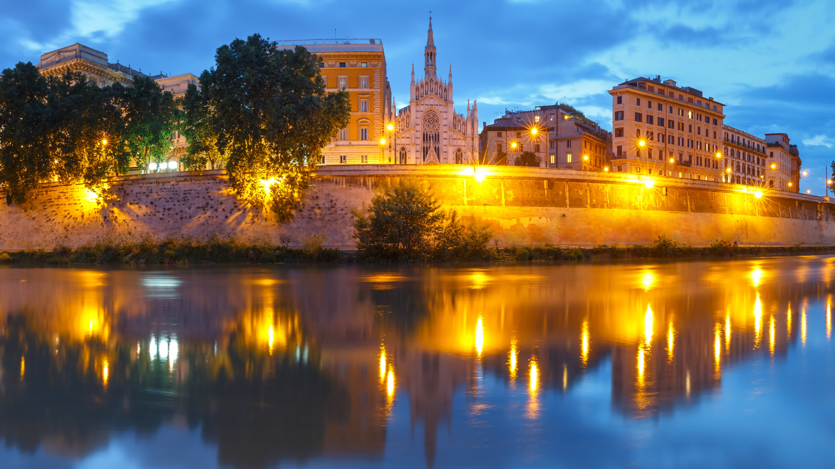 waterway at night with lights and buildings in the background in the Prati Neighborhood In Rome