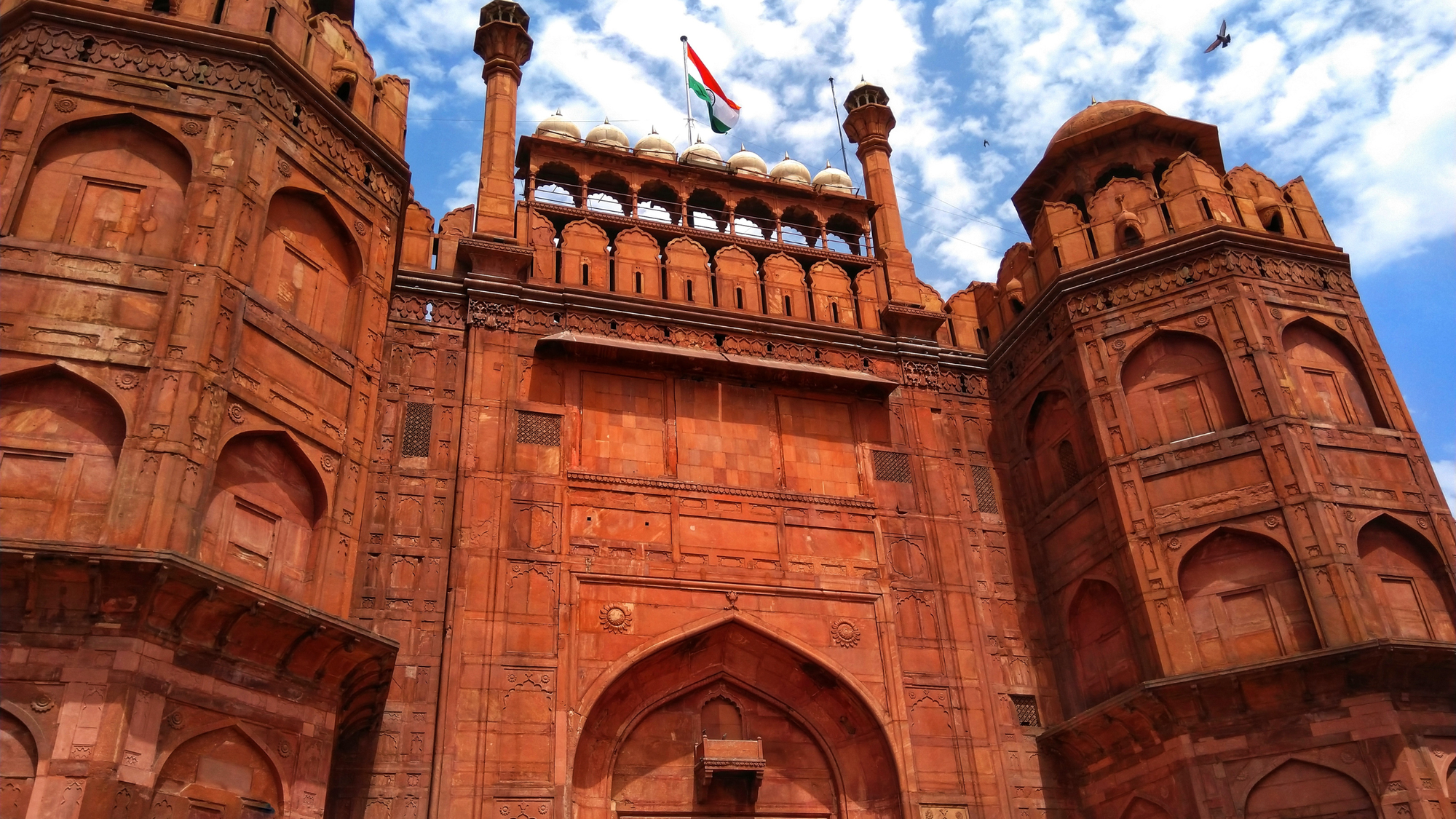 Red Fort in Delhi, India, with towering red sandstone walls and Mughal-style arched entrances.