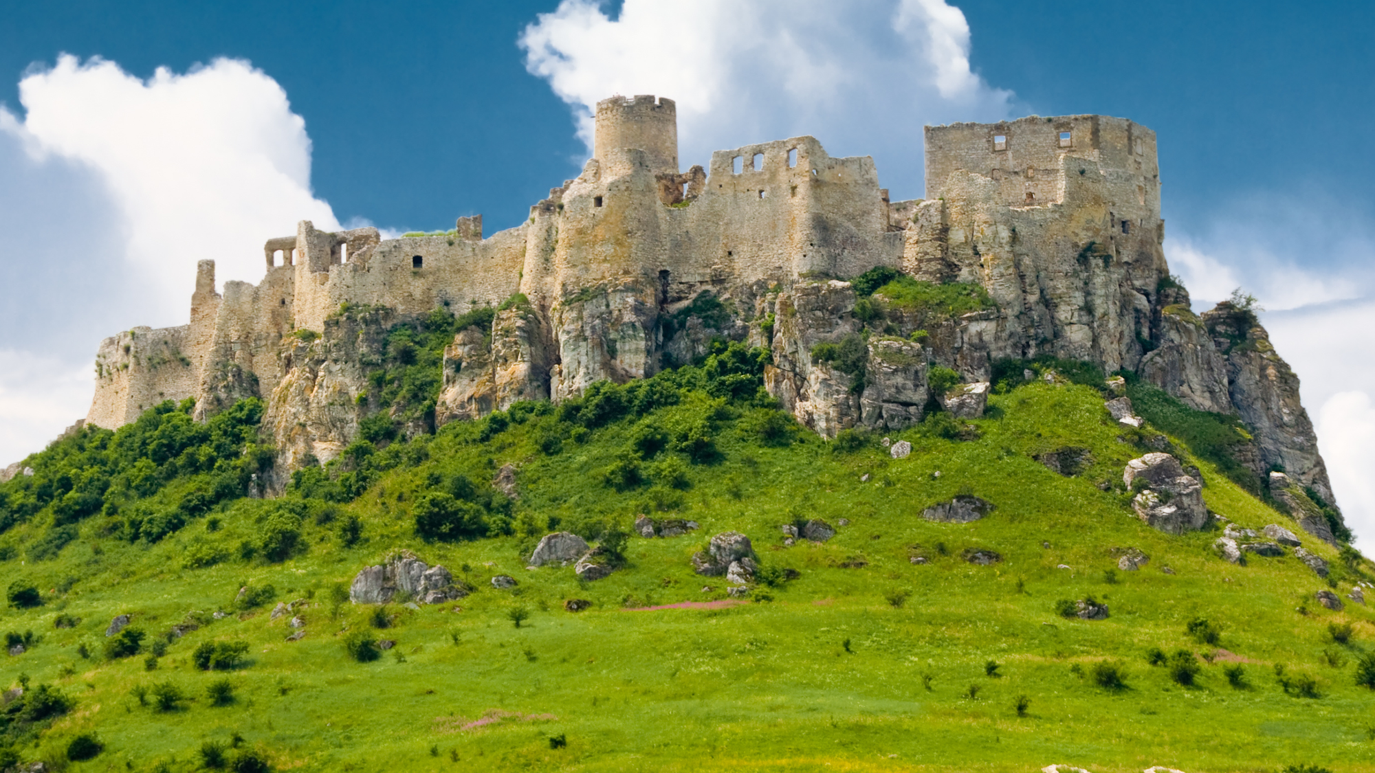 Spis Castle in Slovakia, perched on a hill surrounded by green grass, with its medieval stone walls and towers.