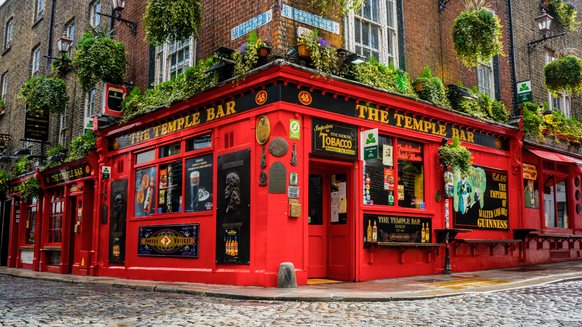 The Temple Bar pub in Dublin, Ireland, with a vibrant red exterior and hanging plants on a cobblestone street corner