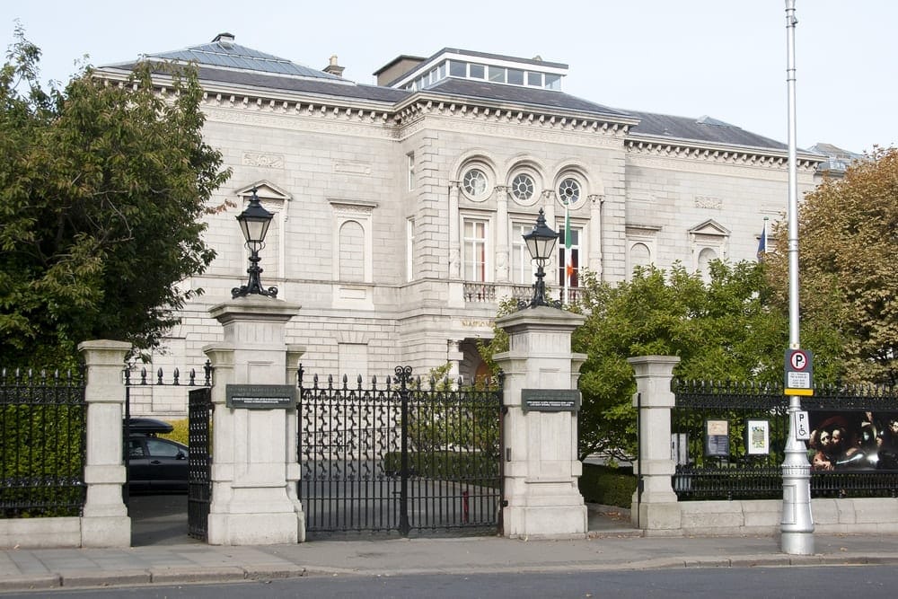 grey brick and mortar building surrounded by trees and a fence at National Gallery of Ireland