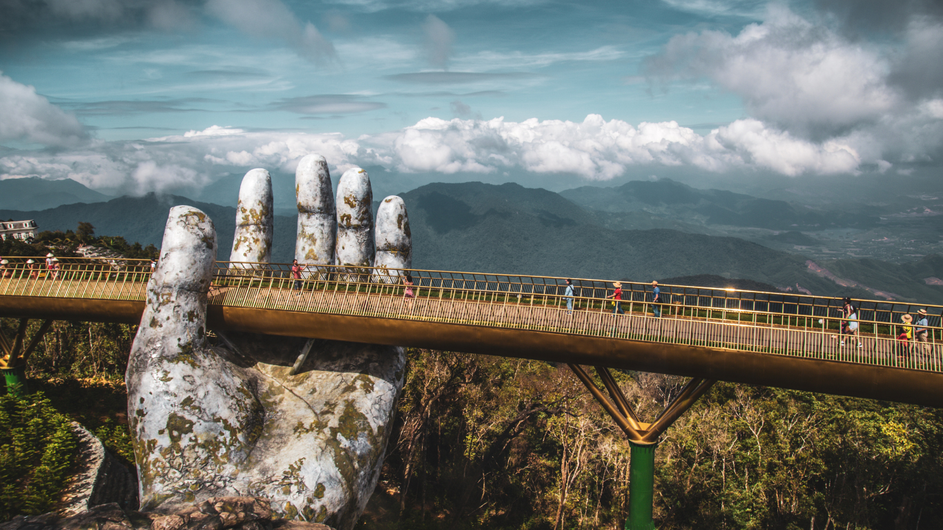 Bridge with a giant hand sculpture appearing to hold it up in Vietnam surrounded by lush mountains