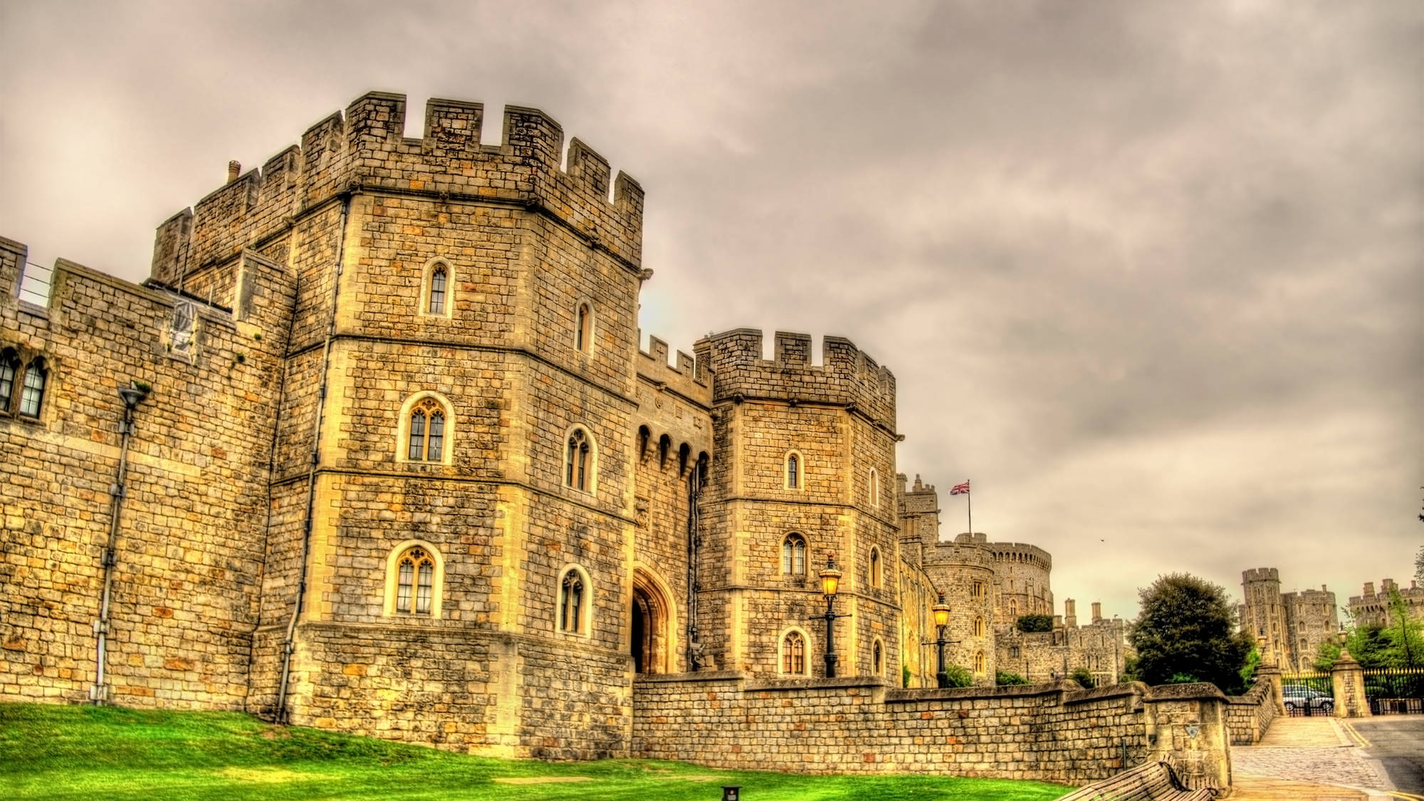 Windsor Castle in England, featuring its imposing stone walls and round towers, with green grass stretching up close to the structure.