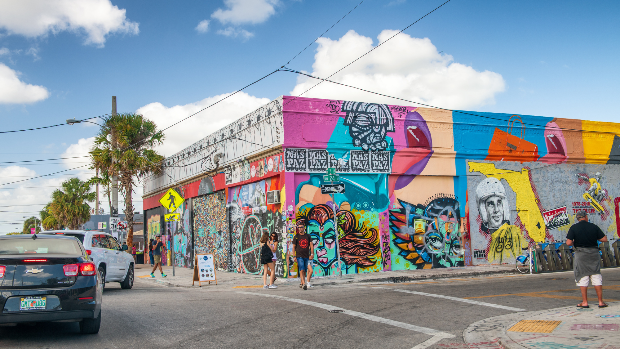 Colorful street art covering buildings in the Wynwood neighborhood of Miami, with people walking and cars driving through the vibrant area.