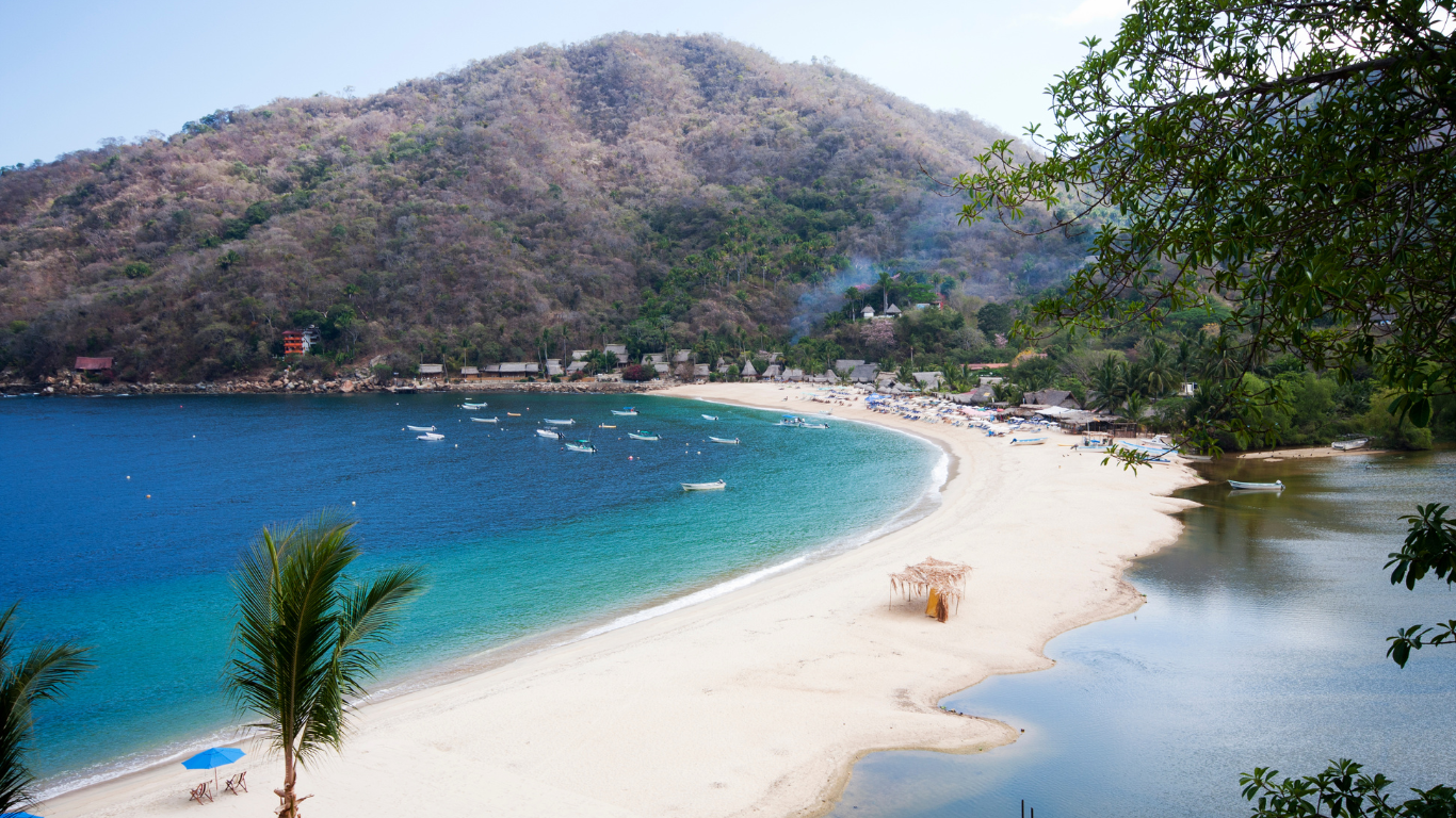 mountain with white sandy beach with boats in the clear blue water in front of it at Yelapa beach in Mexico