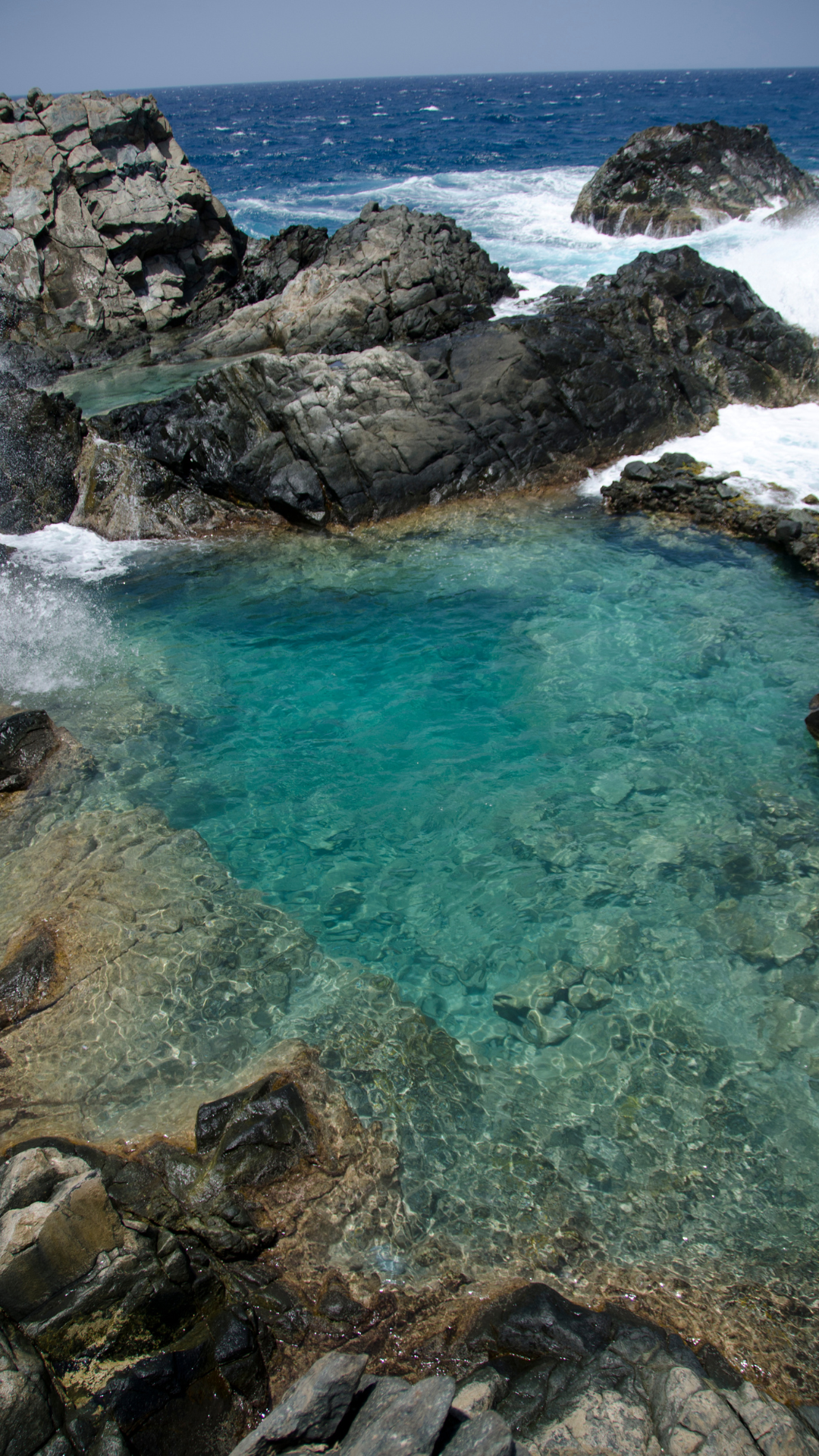 clear blue swimming pool created by enclosure of rocks at the edge of the beach and the water front in Aruba, known as Conchi natural pool