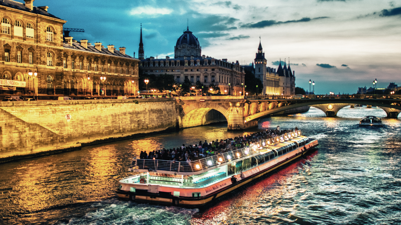 Dinner cruise on the Seine River crossing under a bridge with the city of Paris in the background at sunset