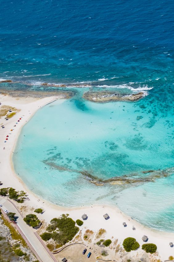 Aruba's Baby Beach is small horseshoe like beach from above, with clear blue water next to a roadway with cars in it