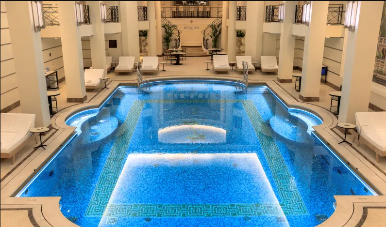 Swimming pool indoors at The Ritz Paris, bright blue surrounded by lounge chairs 