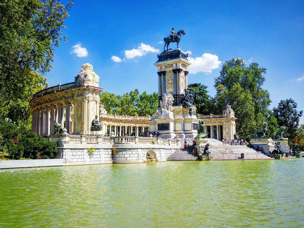 Statues and magnificent structure with visitors relaxing by the water at Retiro Park in Madrid