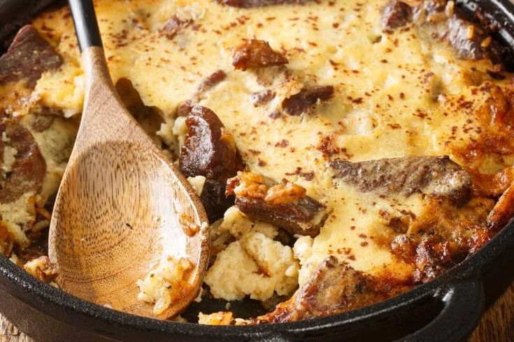 Tavë Kosi  dish in a pan with cheese and beef with a spoon laying on top of it