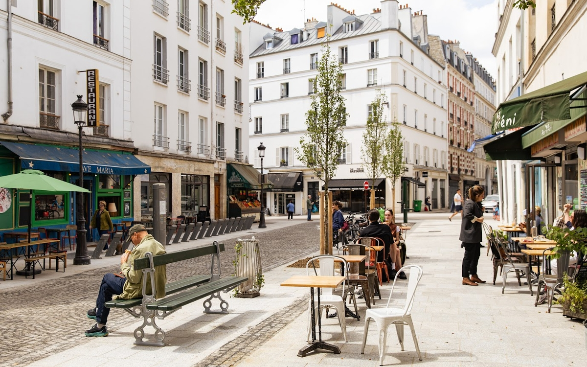 people sitting on benches on Rue Oberkampf in Paris, France surrounded by white buildings and restaurants 