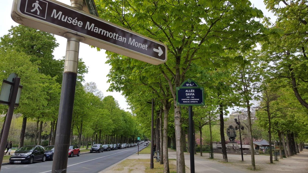 a sign pointing to Musée Marmottan Monet in Paris on a street lined with green leafed trees