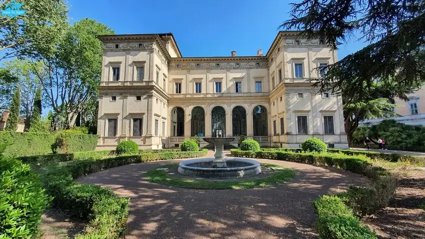 Renaissance villa in Rome, showcasing an elegant two-story structure with symmetrical proportions and a classical facade. The building features large arched windows, intricate frescoes, and a loggia adorned with columns. Set within lush gardens, the villa exudes a sense of refined beauty and tranquility. Its white plastered exterior contrasts with the vibrant greenery, highlighting the architectural harmony of the Renaissance period.