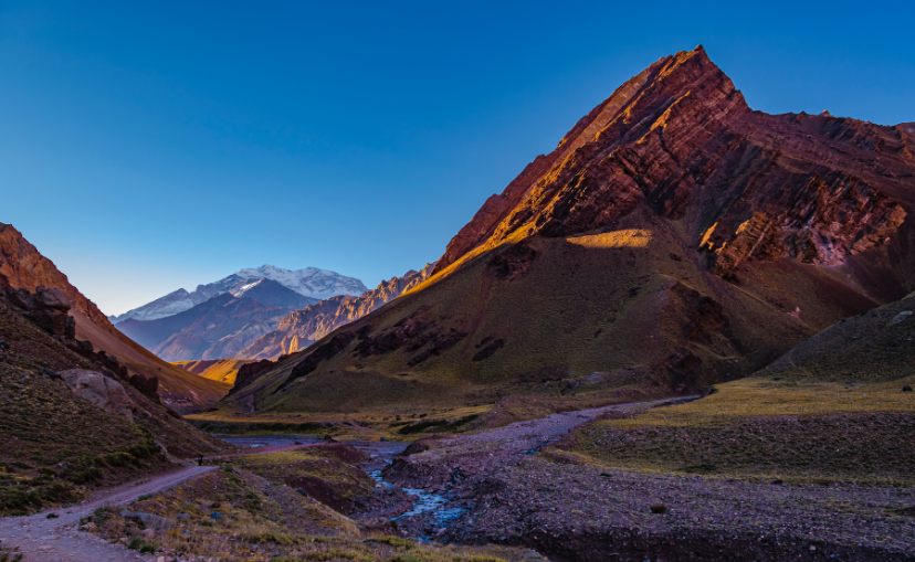 at Aconcagua, we see a beautiful valley with a small stream of water running through what then shoots up into sharp and jagged desert red mountains.