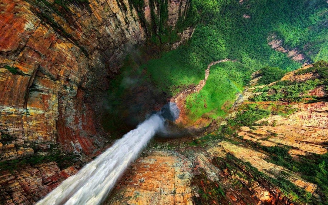 view of a massive water fall from the top looking down at where the fall lands in a lush green jungle 