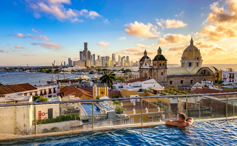 Man in a roof top pool overlooking the beautiful city of Cartagena with sea views in the background.