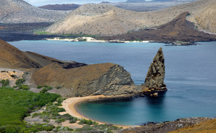 jagged pointy rock coming out of the water near a beach in a bay at the Galápagos Islands.