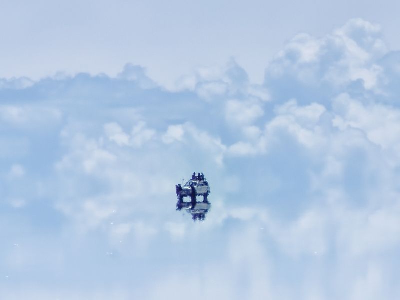 a jeep reflection off of the Salar De Uyuni in Bolivia makes it appear as if the jeep with tourist is floating in the clouds