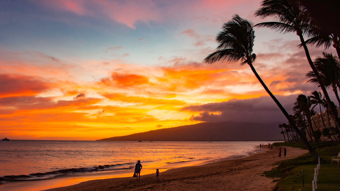 Sunset at the beach in Kihei with a woman and a child walking the shoreline with palm trees blowing in the wind. 