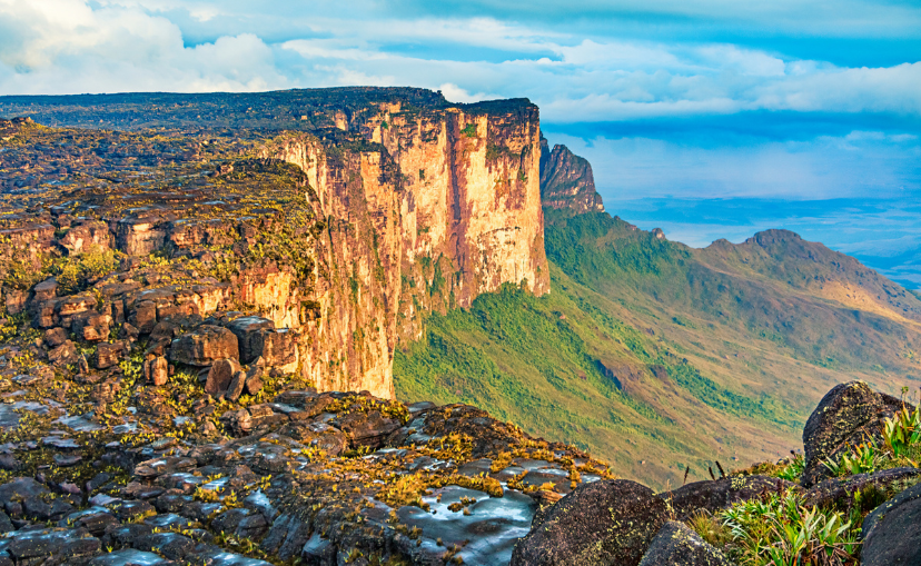 giant flat top mountain that looks like a plateau that has a steep but flat face that leads down to bright green grass.