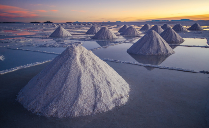 mounds of salt collected at the salt flats in Bolivia with water shining off the waters in the grids of salt