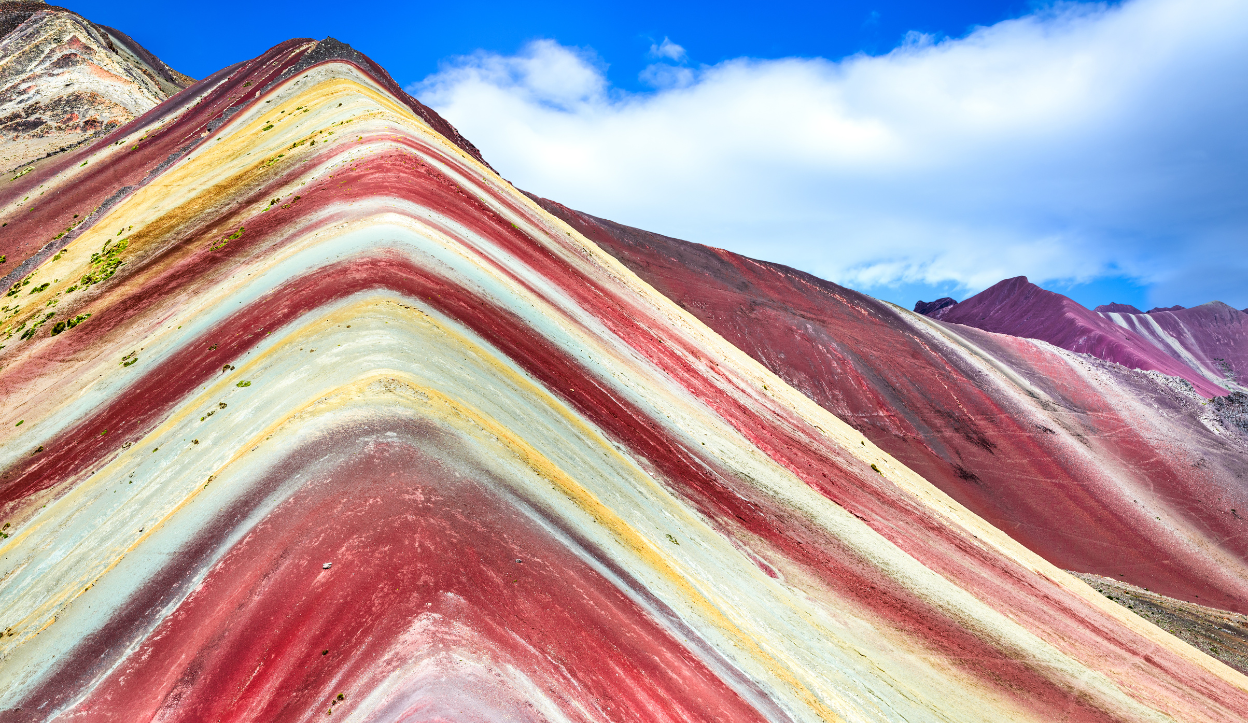 multi colored mountain that has bright colors of red, white and orange going all over it at Vinicunca (Rainbow Mountain)