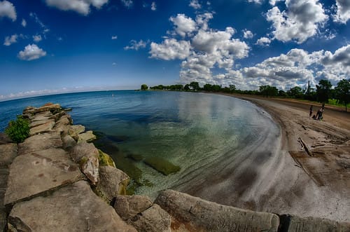 Looking down from a rock ledge showing clear waters and a sandy beach with a few people walking along the beach at Edgewater Beach  in Cleveland, Ohio