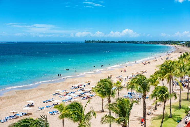 Beautiful Isla Verde Beach in Puerto rico with palm trees blowing in the wind and beach goers playing and laying on the beach. 