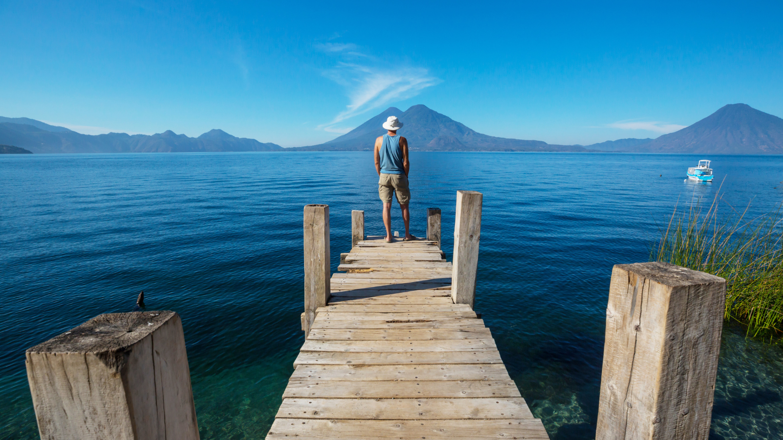 A man standing on a wooded pier in Lake Atitlán, Guatemala with mountains in the background of the lake. 