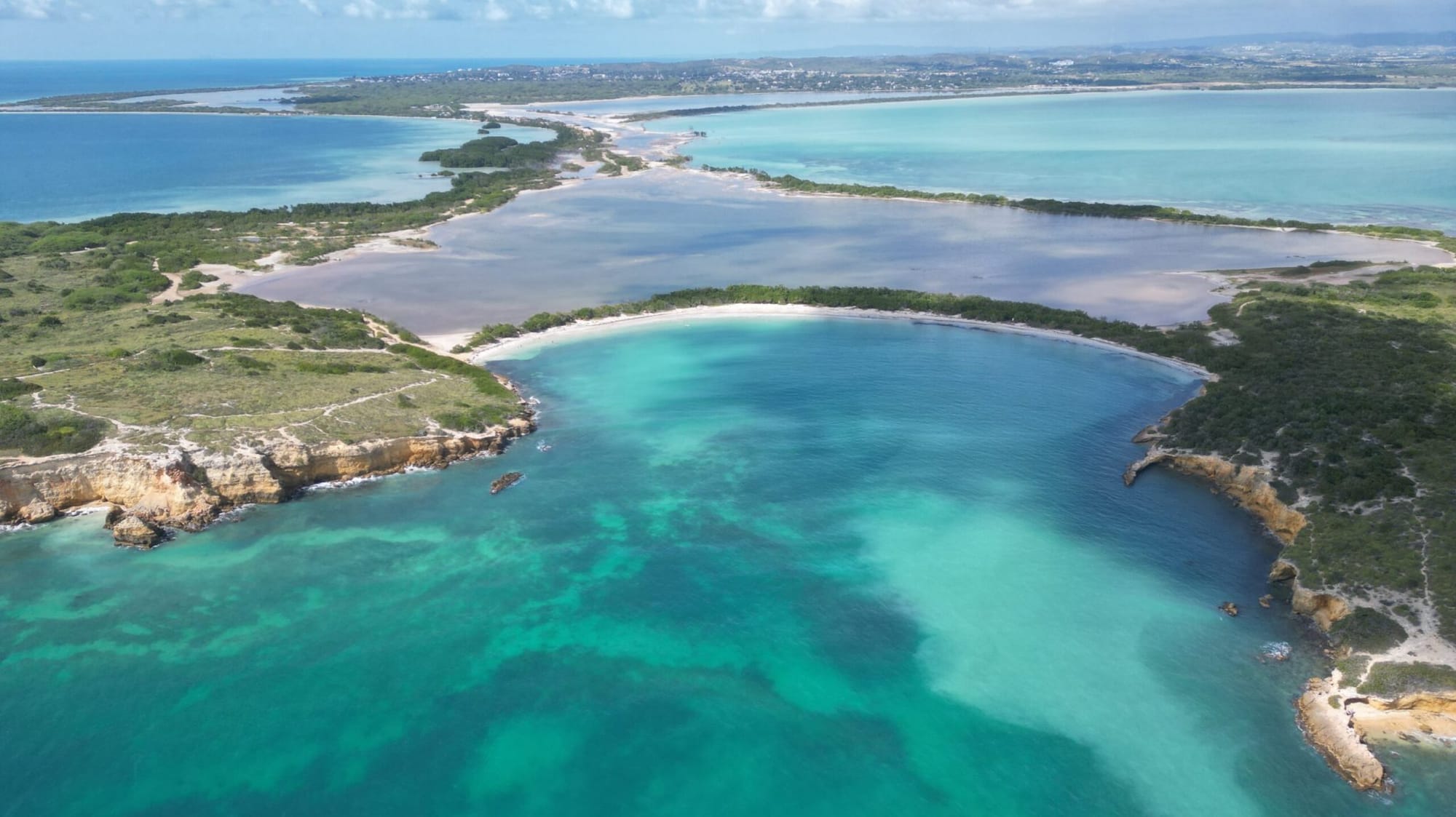 Ariel view of Playa Sucia Beach in Puerto Rico, cliffs on each side of a crescent shaped beach lined with palms and calm clear blue waters. . 